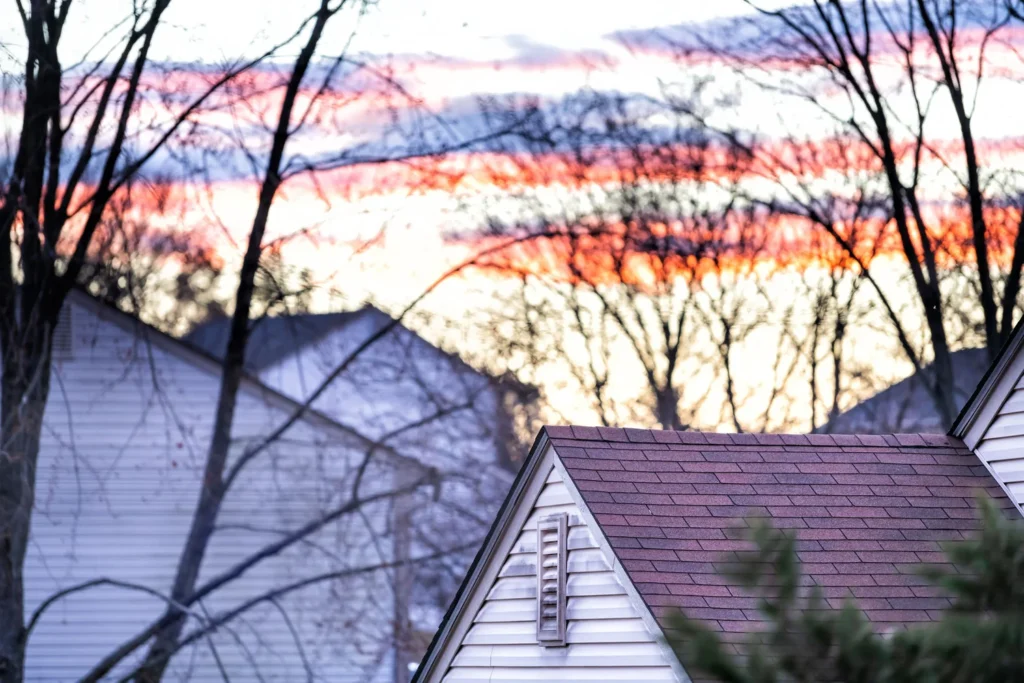 Closeup of roofs, roof, rooftops of homes, houses in residential, suburbs, suburban neighborhood in Virginia, United States during purple, orange, yellow sunset, twilight, dusk