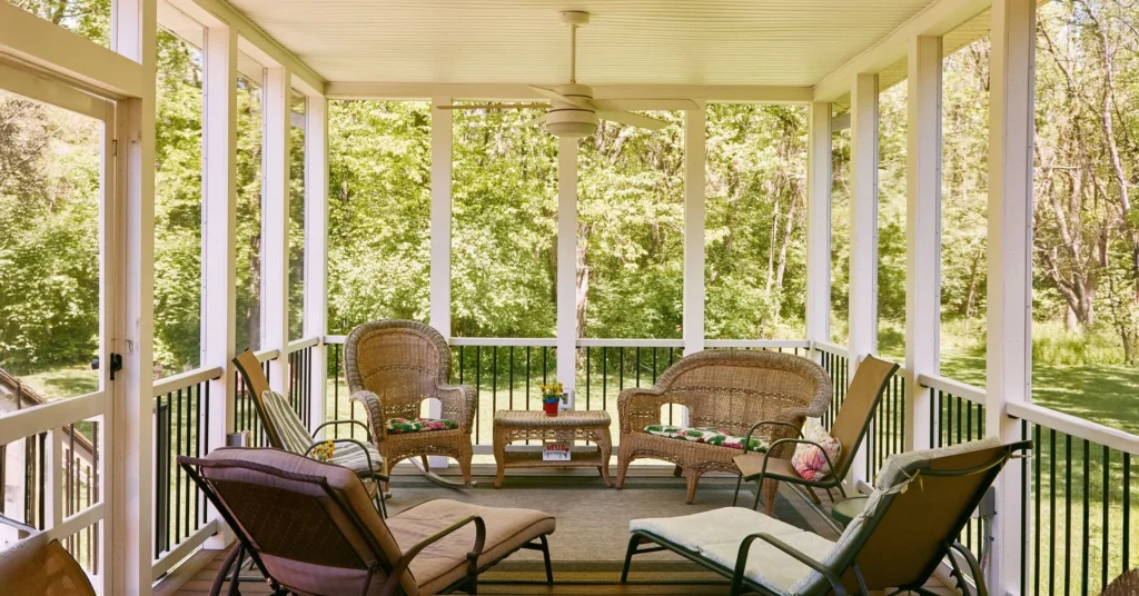 Interior view of screened-in porch with wicker furniture and view of lush greenery outside.