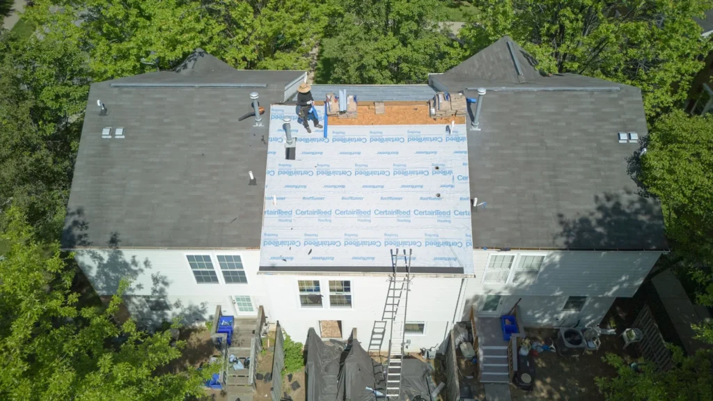 Expert roof installers are laying down CertainTeed Roofing Underlayment on the roof of a townhouse.